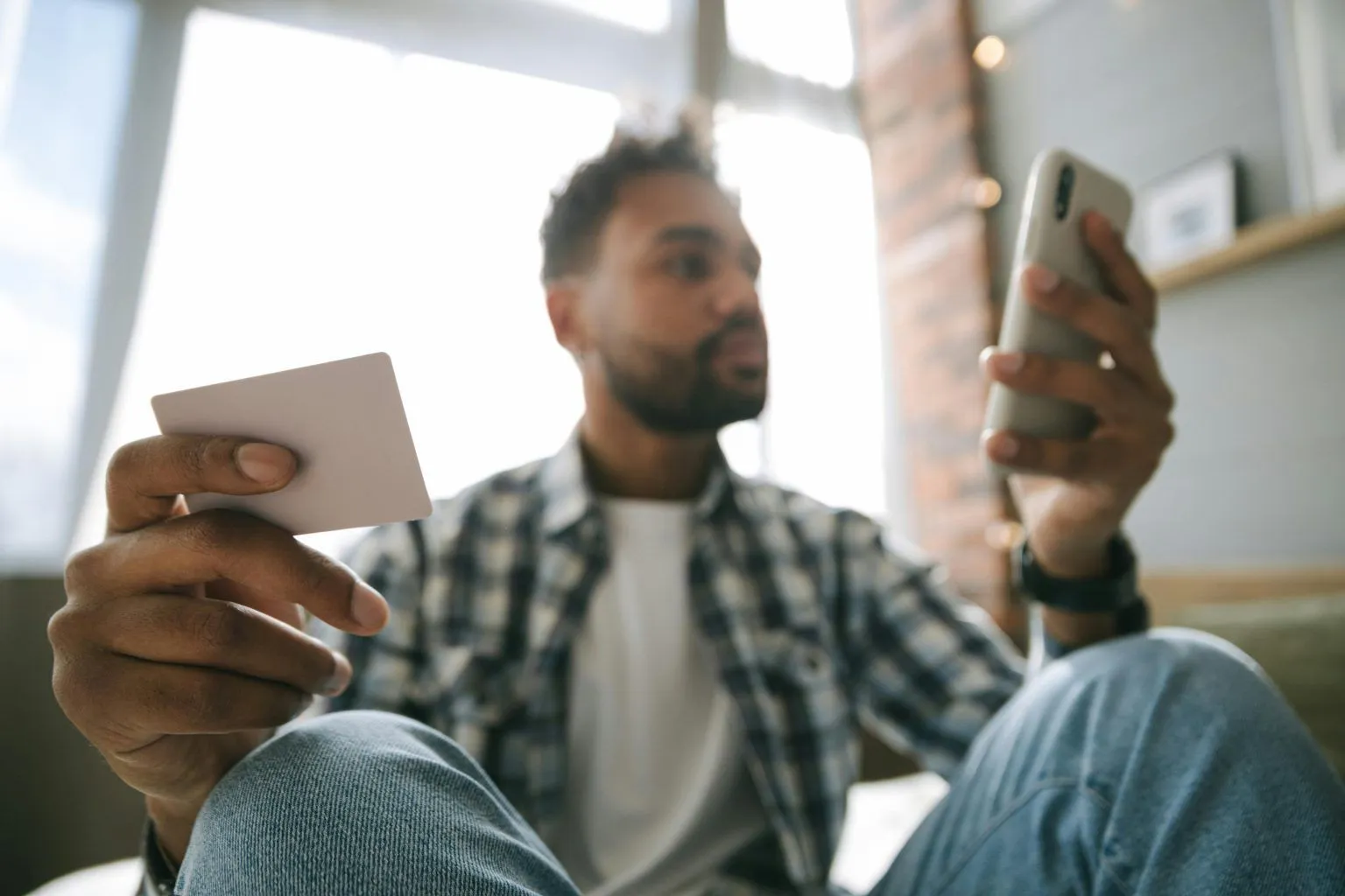 A man checking his card while looking at his phone at home